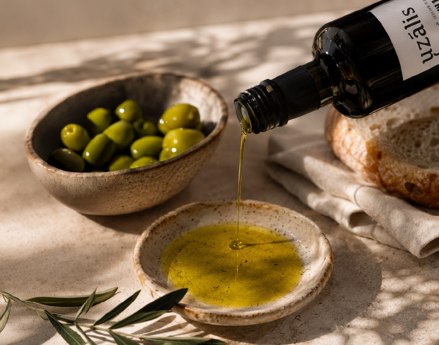 Uzalis Tunisian extra virgin olive oil poured into a ceramic dish beside olives and artisan bread